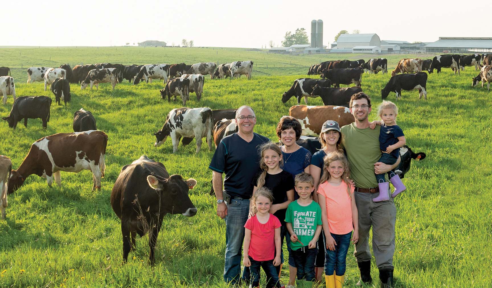 A big and happy family with dozen of cows behind them on a big grass field